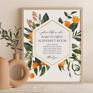 May include: A printable sign with a gold hexagon frame and orange floral illustrations. The text reads "Please help us color Baby's First Alphabet Book. Color a letter, whichever you choose. Sign your name when you've finished, so we know whose is whose. Thank you."
