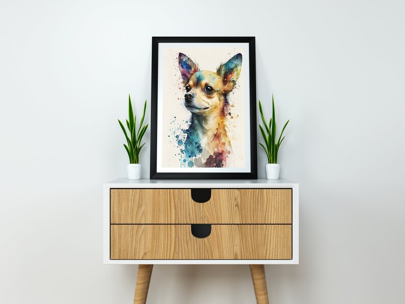 May include: A watercolor painting of a chihuahua dog with colorful splashes of paint in the background. The painting is framed in a black frame and is displayed on a wooden dresser with two drawers.
