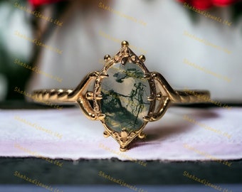 May include: A gold ring with a green and white agate stone set in a detailed, ornate setting. The ring is on a white surface.