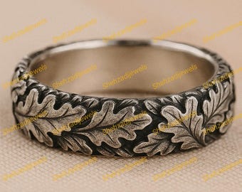 Puede incluir: Un anillo de plata con un detallado diseño de hojas de roble. El anillo tiene un acabado oscuro y oxidado, y las hojas están intrincadamente talladas alrededor de la banda. Una joya.