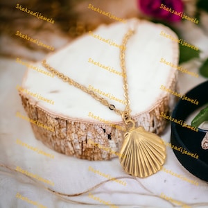May include: A gold chain necklace with a gold seashell pendant. The necklace is displayed on a wooden surface.