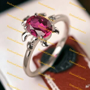 Puede incluir: Un anillo de plata con una piedra preciosa rosa engastada en un diseño de tortuga.