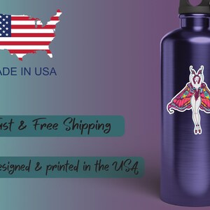 Peut inclure: Une gourde bleu fonc&eacute; avec un autocollant de papillon de nuit color&eacute;. L'autocollant repr&eacute;sente une femme avec des ailes de papillon de nuit dans des tons de rose, de jaune et de bleu. Les mots "MADE IN USA" sont visibles, ainsi qu'une carte des &Eacute;tats-Unis et son drapeau.