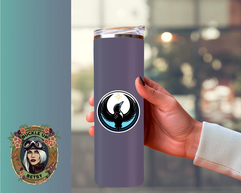 May include: A purple insulated tumbler with a black and white bird emblem. The emblem is a circular design with a bird silhouette, a crescent moon, and a star. The tumbler is held by a person.