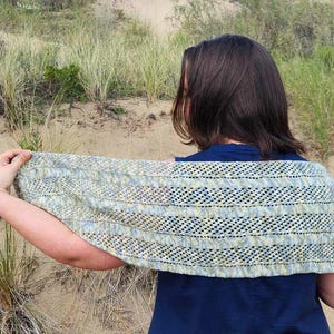May include: A person wearing a blue shirt and a light blue, yellow, and green crocheted shawl with a lacy pattern.