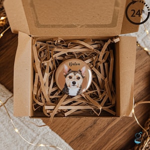 May include: A round button with a dog portrait and the name "Jalea" in a brown gift box with shredded paper. The button has a tan background with a dog's face. The box is brown and has a 24-hour delivery icon.