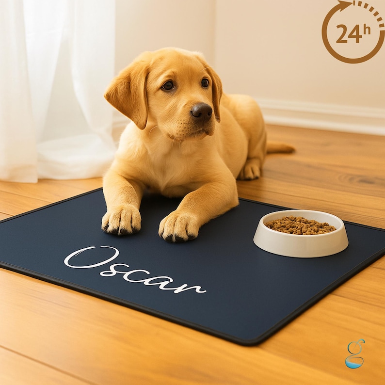 May include: A golden Labrador puppy lies on a navy blue pet feeding mat. The mat has the name "Oscar" in white script. A white bowl filled with dog food sits to the right of the mat. A 24-hour icon is in the upper right corner.