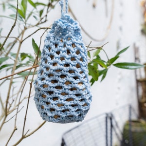 Peut inclure: Un mangeoire à oiseaux en crochet bleu clair suspendu à une branche d'arbre. La mangeoire est remplie de graines pour oiseaux.