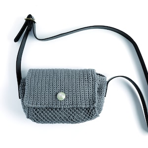 May include: A gray crocheted crossbody bag with a black leather strap and a white button.