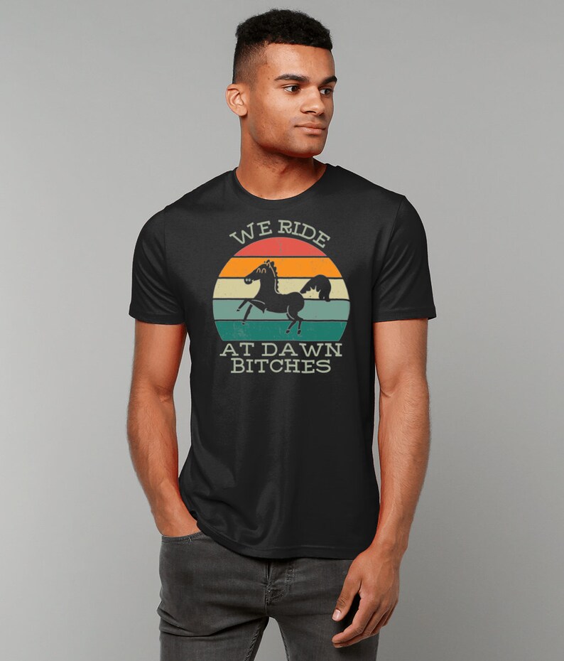 May include: Black t-shirt with a vintage-style graphic of a black horse running in front of a sunset. The graphic says "We Ride At Dawn Bitches".