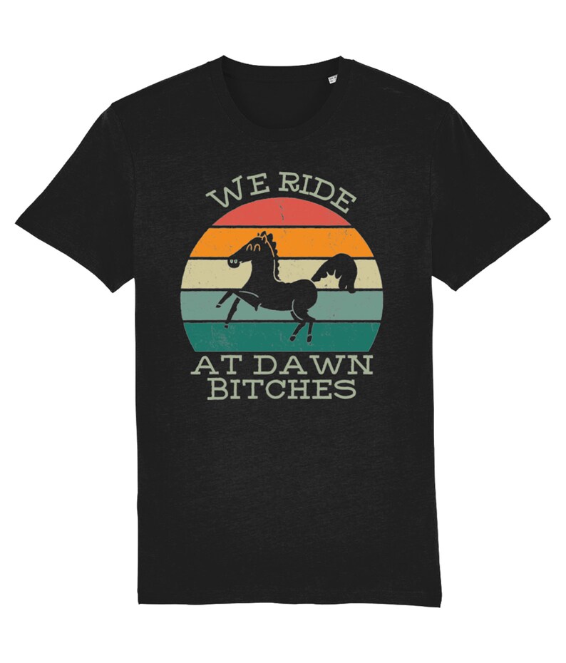 May include: Black t-shirt with a vintage-style sunset graphic and the text "WE RIDE AT DAWN BITCHES". A black silhouette of a horse is in the center of the graphic.