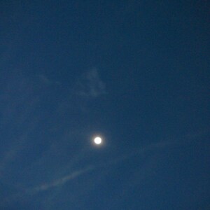 May include: A bright white moon in a dark blue sky with wispy white clouds.
