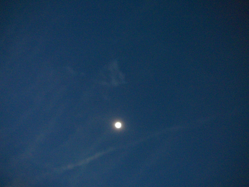 May include: A bright white moon in a dark blue sky with wispy white clouds.