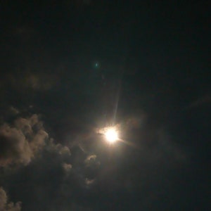 May include: A bright sun shining through dark clouds in the sky.