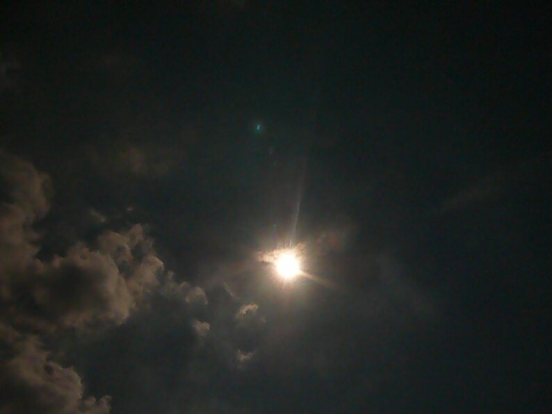 May include: A bright sun shining through dark clouds in the sky.