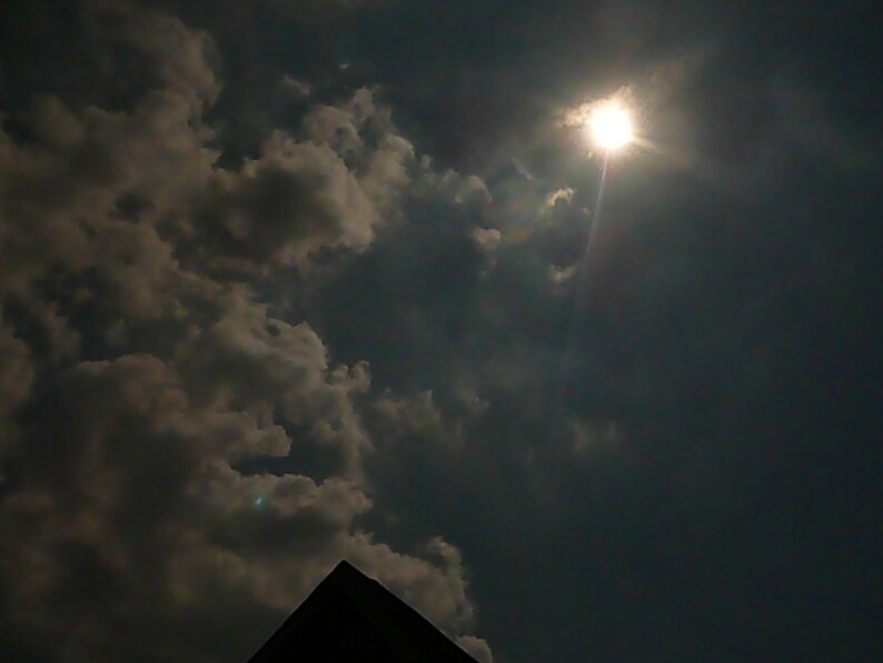 May include: A bright sun shines through dark clouds in the sky.