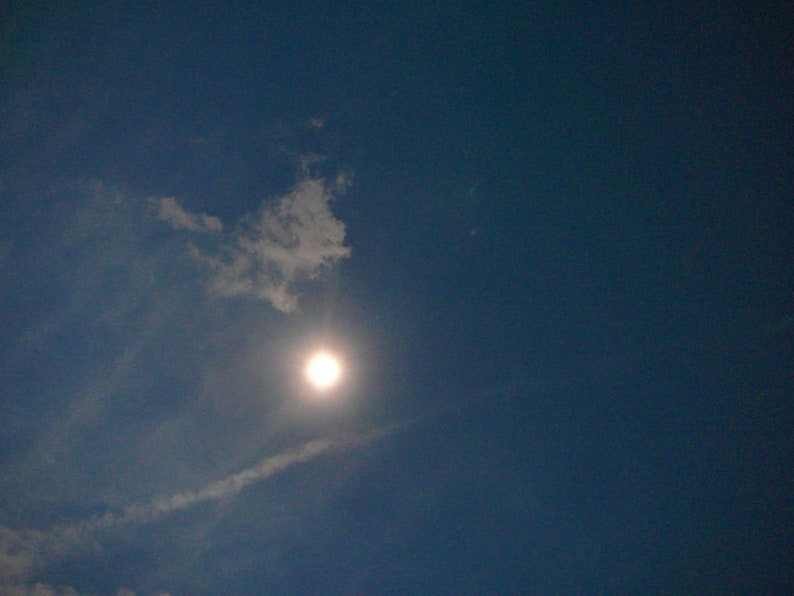 May include: A bright, white sun shining through a light blue sky with wispy white clouds.