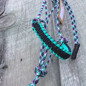 May include: A turquoise, black, and purple braided rope halter for horses. The halter is made of a thick, durable rope and has a unique braided design.