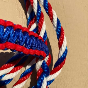 May include: Close-up of a red, white, and blue braided rope. The rope is made of three strands of rope, each with a different color. The rope is twisted together to create a unique pattern.