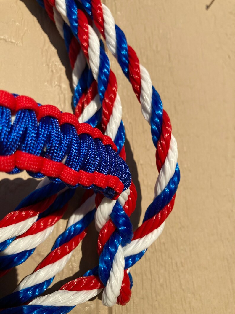 May include: Close-up of a red, white, and blue braided rope. The rope is made of three strands of rope, each with a different color. The rope is twisted together to create a unique pattern.