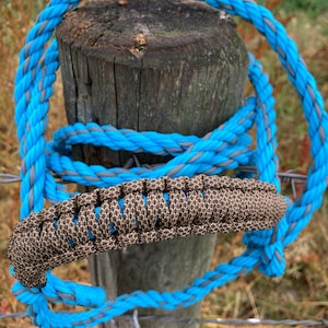 Puede incluir: Un cabezada de cuerda azul y gris con un mango trenzado marrón. La cabezada está envuelta alrededor de un poste de madera.