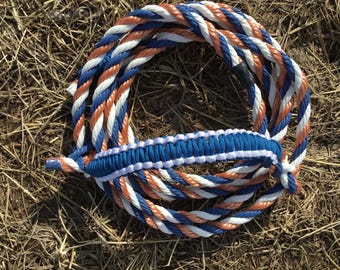 May include: A coiled rope halter in blue, white, and orange. The halter features a braided noseband and a loop for the lead rope. The rope is made of durable material, suitable for equine use.