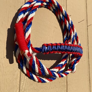 May include: A red, white, and blue braided rope with a blue paracord handle. The rope is coiled and hanging on a wooden wall.