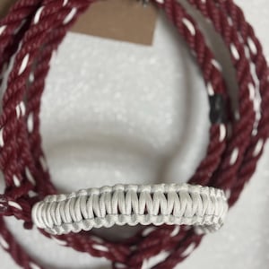 May include: A white braided rope with a red and white rope wrapped around it. The white rope has a braided loop.