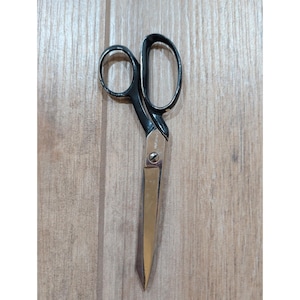 May include: A pair of sewing scissors featuring black handles and silver-toned metal blades. The scissors are joined by a central screw and have a small, pointed tip. The black coating on the handles shows minor signs of wear and chipping.