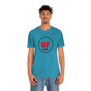Op de afbeelding: Een turquoise blauw t-shirt met een zwart en rood logo met de tekst "MF GAMING" in een cirkel met een doelwitontwerp.