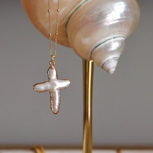 May include: A gold necklace with a white pearl cross pendant displayed on a gold seashell stand.