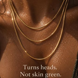 May include: A layered gold-toned snake chain necklace set featuring three delicate strands of varying lengths. The text on the image reads: Turns heads. Not skin green. Waterproof | Lifetime Guarantee. The chains have a smooth, reflective finish.
