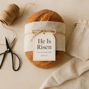 May include: A loaf of bread wrapped in beige fabric with a brown twine bow and a white tag that reads "He Is Risen, I am the bread of life, John 6:35".