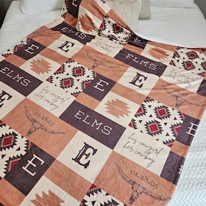 May include: A personalized blanket with a patchwork design in shades of brown, tan, and burgundy. The blanket features the name "ELMS", the letter "E", a steer skull, and the text "his cowgirl/her cowboy" and the date "01.28.05".