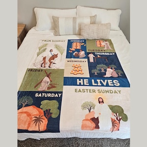 May include: A white throw blanket with a blue and green design depicting the days of Holy Week and Easter Sunday. The blanket features illustrations of Jesus and scenes from the Bible. The text on the blanket reads "Palm Sunday", "Monday", "Tuesday", "Wednesday", "Thursday", "Friday", "Saturday", "He Lives", and "Easter Sunday".