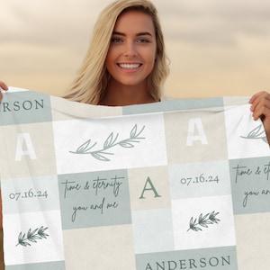 May include: A personalized light blue and beige blanket with the text "Time & Eternity You and Me" and the date "07.16.24" printed on it. The blanket also features a stylized floral design and the letter "A" repeated throughout.