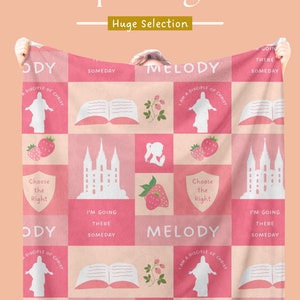 Op de afbeelding: Roze en wit patroon deken met religieuze en inspirerende beelden. De deken heeft vierkanten met aardbeien, open boeken en de tekst "I'm going there someday". De deken wordt door twee handen omhoog gehouden.