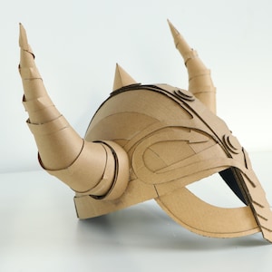 May include: A handmade cardboard helmet with large, spiraling horns and intricate layered details. The helmet is a natural tan color and appears to be constructed from multiple pieces of corrugated cardboard, suggesting a DIY or costume theme.