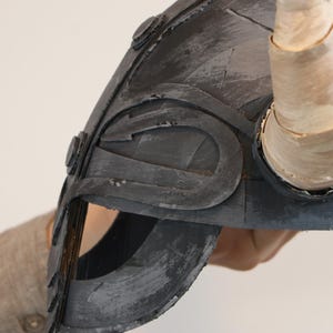 May include: A gray Viking helmet with a curved design and a single horn. The helmet has a distressed, textured appearance with visible brushstrokes. The horn is a light beige color.