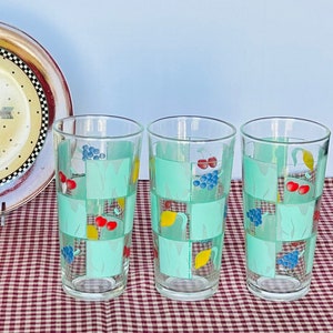 May include: Set of three clear glass drinking glasses with a green and white checkered pattern and colorful fruit designs. The glasses have a vintage look.