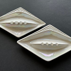 May include: Two white ceramic diamond-shaped ashtrays with a raised lip and a row of five indentations in the center.