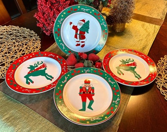 May include: Four white ceramic Christmas plates with green and red trim. The plates feature a reindeer, Santa Claus, a nutcracker, and a second reindeer. The plates are perfect for a holiday table setting.