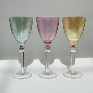 May include: Three wine glasses with gold rims. The glasses are clear and have a light blue, pink, and yellow tint.