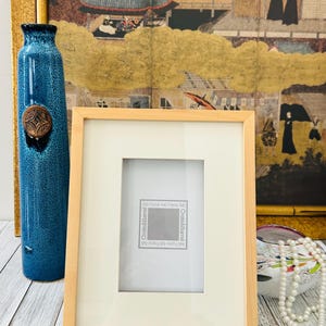 May include: A rectangular wooden picture frame with a cream-colored mat and a clear glass cover. The frame is labeled "Crate & Barrel" and is designed for a 4x6 inch photo. A blue vase and a decorative painting are in the background.