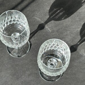 Puede incluir: Dos copas de vino de vidrio transparente con un patr&oacute;n texturizado en forma de diamante. Las copas est&aacute;n vac&iacute;as y est&aacute;n sobre una superficie gris oscuro.