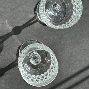 Puede incluir: Dos vasos de vidrio transparente con tallo y un patr&oacute;n texturizado en el cuenco y el tallo. Los vasos est&aacute;n vac&iacute;os y est&aacute;n sobre una superficie gris oscuro.