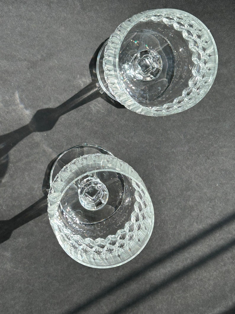 Puede incluir: Dos vasos de vidrio transparente con tallo y un patr&oacute;n texturizado en el cuenco y el tallo. Los vasos est&aacute;n vac&iacute;os y est&aacute;n sobre una superficie gris oscuro.