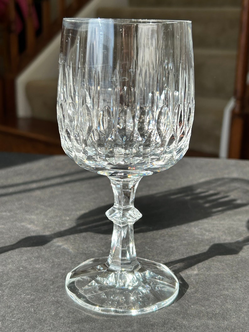 Puede incluir: Una copa de vino de cristal tallado transparente. La copa tiene un tallo alto y una base redonda.