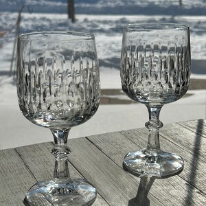 Puede incluir: Dos copas de vino de cristal transparente con un dise&ntilde;o de cristal tallado. Las copas est&aacute;n sobre una mesa de madera.