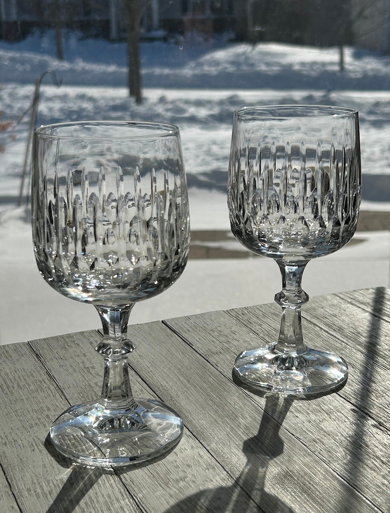 Puede incluir: Dos copas de vino de cristal transparente con un dise&ntilde;o de cristal tallado. Las copas est&aacute;n sobre una mesa de madera.